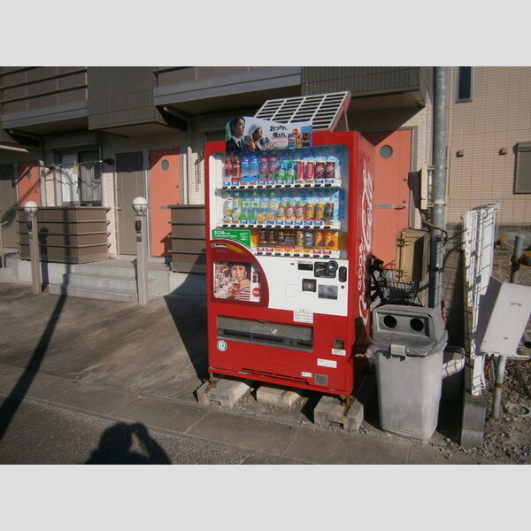 リヴェール 建物の前に飲料水の自動販売機があります。